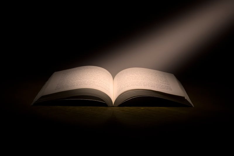 An open book illuminated by a beam of light in darkness — wisdom, knowledge, and revelation